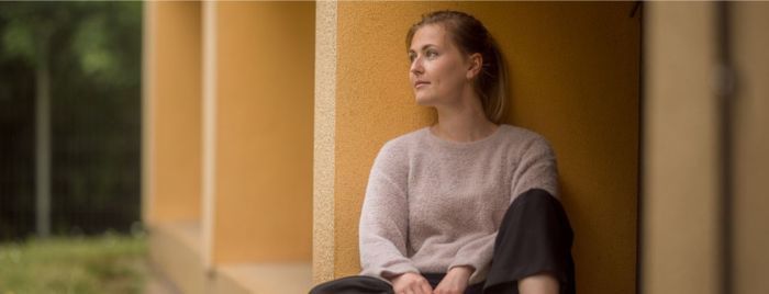 Frau sitz auf Boden, angelehnt an Wand und schaut in die Ferne.